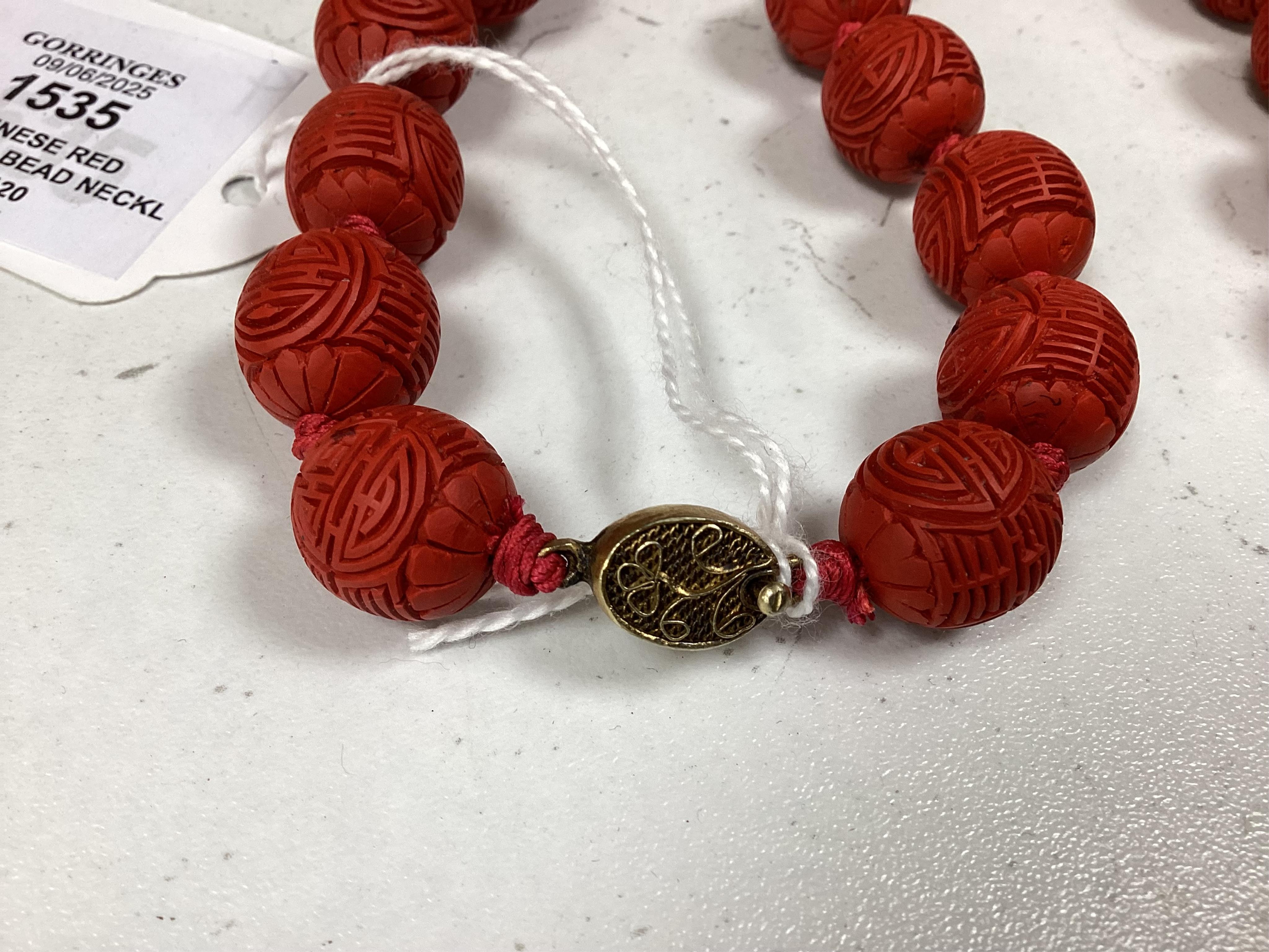 A Chinese red lacquered bead necklace and a bowenite jade figure of a cat